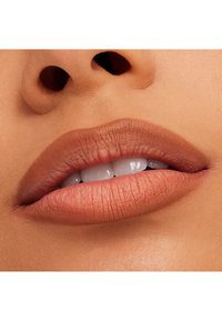 Närbild av läppar med matt nude-finish, slät textur, väldefinierad form och subtil naturlig nyans, som avslöjar vita tänder.