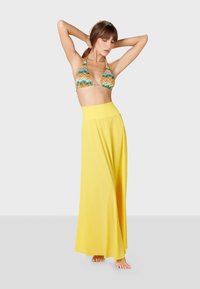 Top de bikini con un patrón de zigzag multicolor, combinado con una fluida falda maxi amarilla. La prenda presenta una cintura alta y una tela suave.