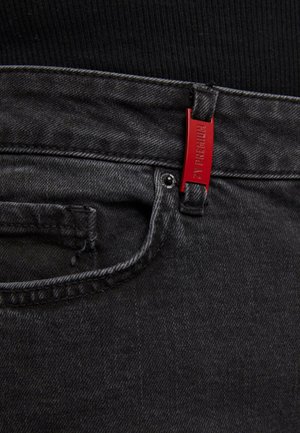 Black denim jeans with a textured finish, featuring a red branded tag on the waistband and a front pocket with stitched detailing.