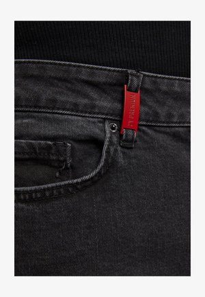 Sorte denim jeans med en tekstureret overflade, prydet med et rødt mærke på linningen og en forlommer med stikdetaljer.