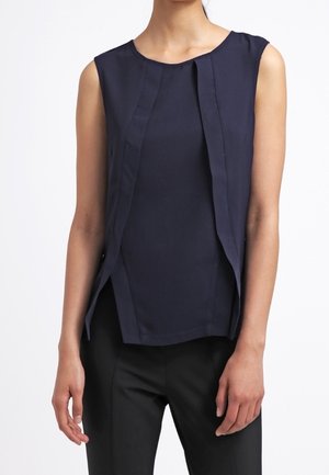 Niebieska bezrękawnikowa bluzka z pionowymi plisowanymi detalami, noszona z czarnymi spodniami, pokazana od środka tułowia do szyi, stojąca na białym tle.