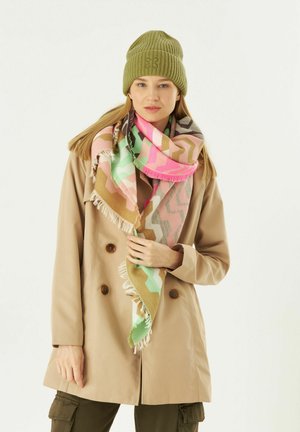 Beige Doppelreiher-Mantel, gemusterter, mehrfarbiger Schal in Rosa, Grün und Braun, grüner, gerippter Strickmütze. Fransen an den Schalenden.