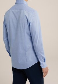 Camisa de manga larga azul clara hecha de un tejido suave, con cuello tipo camisa, puños con botones y un diseño trasero bien ajustado.