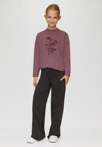 Langärmliger, mauvefarbener Sweatshirt mit einem floralen Grafikdesign und dem Text "dreamy". Kombiniert mit lockeren schwarzen Hosen und weißen Sneakers.
