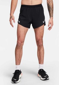 Shorts de sport noirs en tissu respirant, dotés d'une taille en mesh et d'accents de logo Nike blancs sur les côtés.