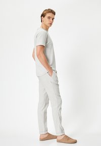 T-shirt corto grigio chiaro con texture, abbinato a pantaloni grigio chiaro e scarpe slip-on beige. Design minimalista con vestibilità rilassata.