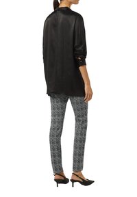 Schwarze Satin-Hemd mit langen Ärmeln und umgeschlagenen Manschetten, kombiniert mit eng anliegenden Hosen im schwarz-weißen Fischgrätenmuster und schwarzen Slingback-Absätzen.