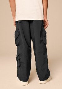 Svarta cargobyxor gjorda av ett lätt material, med flera sidofickor och en lös passform, i kombination med vita sneakers.