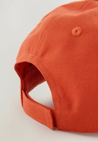 Oranje katoenen pet met een gebogen klep en een verstelbare band aan de achterkant. Kenmerkt zichtbare stiksels en een gestructureerde stofafwerking.