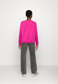 Fuchsiový svetr s dlouhými rukávy, kulatým výstřihem a žebrovaným lemem, doplněný o šedé džíny s širokými nohavicemi a vysokým pasem a barevné tenisky.