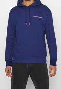 Sudadera azul marino de tejido suave, con un logo rosa en el pecho y cordones rosa en contraste. Puños y dobladillos de canalé.