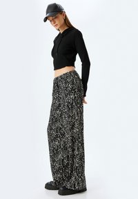 Zwarte, cropped hoodie met ribbelstructuur, gecombineerd met losse, zwart-wit gestreepte wijde broek. Afgemaakt met een zwarte pet en chunky schoenen.