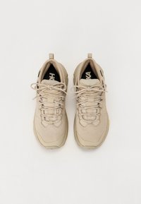 Pantofi sport bej cu upper texturat, vârf rotund și șireturi plate. Au un tab cu care se poate trage și o talpă interioară cu logo contrastant negru.