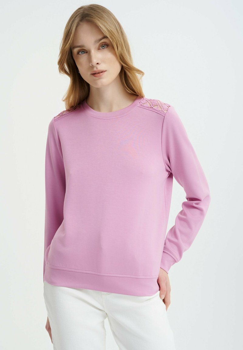 Felpa rosa chiaro con maniche lunghe, collo tondo e dettagli in pizzo decorativi sulle spalle. Realizzata in un tessuto morbido e elasticizzato.