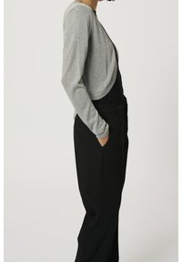 Cardigan court argent scintillant à manches longues, design drapé, porté sur une tenue noire, affichant une finition lisse et texturée.