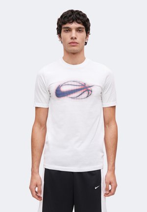 Jeune homme portant un t-shirt blanc avec un logo flou de basketball et swoosh et un short noir avec un petit logo swoosh blanc.