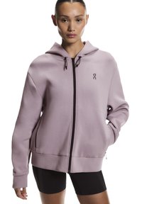 Sweat à capuche zippé violet clair en tissu doux, doté d'une capuche, de poches avant et de cordons de serrage ainsi que de détails de fermeture éclair noirs.