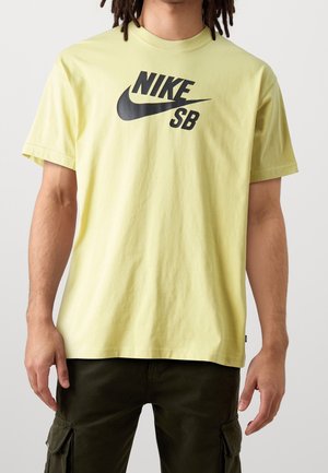 Gelbes Baumwoll-T-Shirt mit einem auffälligen schwarzen Nike SB-Logo auf der Brust. Kurze Ärmel und lockere Passform.