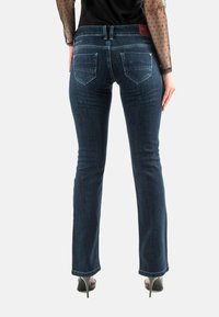 Jeans de mezclilla azul oscuro acampanados con una cintura de media altura, dos bolsillos traseros y una etiqueta de cuero en la cinturilla. Textura suave, ajuste entallado.