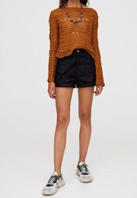 Maglione all'uncinetto di colore ruggine con maniche lunghe, abbinato a pantaloni shorts neri a vita alta. Completano l'outfit delle sneakers chunky multicolori.