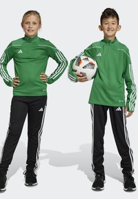 Grüne sportliche Zip-Up-Tops mit weißen Streifen und schwarze Hosen mit weißen Seitenstreifen, getragen von zwei Kindern, von denen eines einen Fußball hält.