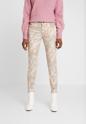 Pantalons ajustés à motif floral dans des couleurs pastel avec une base beige clair. Comprend des accessoires décoratifs à la taille et des détails cloutés aux chevilles.