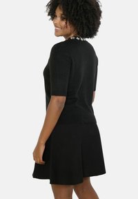 Čierny pletený sveter s krátkymi rukávmi, s textúrovaným dizajnom a dekoratívnymi detailmi pri výstrihu. V páre s ladiacou sukňou.