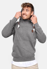Grauer Hoodie mit hohem Kragen und Kordeln, versehen mit einem strukturierten Muster und einem Lederlogo-Patch auf der Brust. Weicher Stoff.