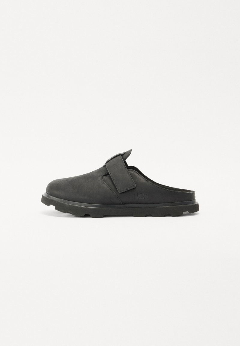 Zapatos negros sin cordones de ante con una suela acolchada, que presentan una correa ancha en la parte superior y una suela plana y texturizada para un mejor agarre.