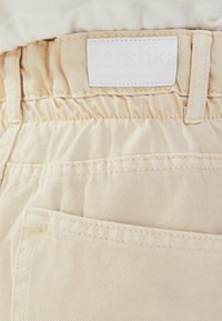 Närbild av beiga denimbyxor med bakficka, elastisk midja och vit Bershka-märkesetikett ovanför.