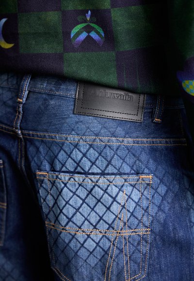 Blue denim jeans with diamond-patterned texture, featuring contrasting orange stitching and a black leather patch labeled "Ahluwalia."