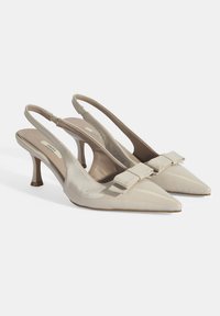 Talons aiguilles en cuir verni beige avec un bout pointu, un talon stiletto de 3 pouces et un accent de nœud décoratif sur le cou-de-pied.