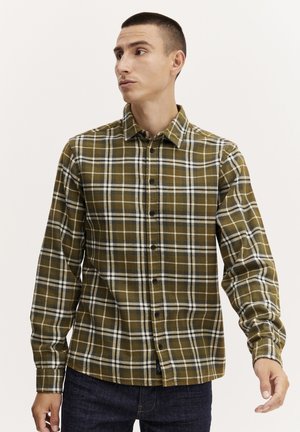 Camisa a cuadros en verde, marrón y blanco, con mangas largas, cierre de botones en el frente y cuello puntiagudo. Hecha de una tela suave, presenta un corte relajado.