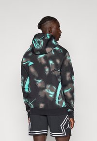 Sudadera con capucha en negro con un patrón abstracto en turquesa y beige. Presenta un corte holgado, puños de canalé y un bolsillo tipo canguro.