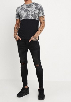 Zwart-grijs T-shirt met korte mouwen en bloemenpatroon op de bovenste helft; gecombineerd met zwarte skinny jeans en zwarte sneakers.