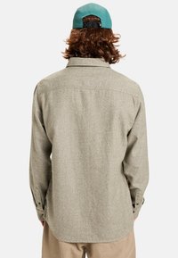 Lichtgrijze flanellen shirt met een ontspannen pasvorm, zichtbare textuur, knopenmanchetten en een gebogen zoom. Draag een teal pet.