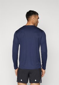 Mørkeblå langærmet træningsshirt lavet af letvægtsmateriale, med rund halsudskæring og fladlock-sømme, parret med sorte shorts.