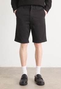 Shorts noirs en tissu mélangé de coton, avec une taille plate, des poches latérales et une coupe régulière, associés à des chaussettes blanches et des chaussures noires.