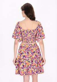Blomster crop top og nederdel sæt med smocket bodice, puffede ærmer og en lagdelt nederdel i livlige farver som lilla, gul og grøn.