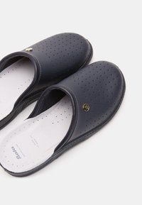 Tengerész stílusú, perforált szintetikus anyagból készült slip-on cipők, fehér talpbetéttel és arany logóval a felsőrészen.