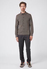 Camisa de manga larga con un patrón geométrico en colores oscuros, cuello abotonado, combinada con pantalones de rayas grises y zapatillas con colores de acento.