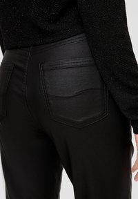 Pantalons noirs taille haute en tissu lisse avec poches arrière. La ceinture est soigneusement cousue, avec des détails subtils le long des poches.