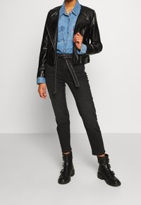 Giacca da biker nera in finta pelle sopra una camicia di jeans azzurri chiari, abbinata a jeans neri a vita alta e stivaletti neri con fibbie.
