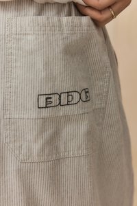 Lys beige stof med smalle vertikale blå striber, der har en baglomme med sort "EDGE" broderi. Glat tekstur.