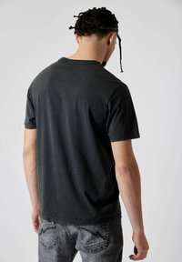T-shirt en coton noir avec un col rond, des manches courtes et une coupe décontractée. Le tissu semble doux avec une légère texture.