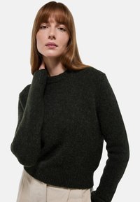 Pull en tricot texturé vert foncé avec un col rond et des manches longues, présentant un design court et une bordure côtelée.