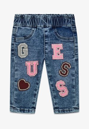 Niebieskie jeansowe spodnie dla maluchów z elastycznym paskiem w talii oraz ozdobnymi naszywkami z napisem „GUESS” i w kształcie serca na przednich nogawkach.
