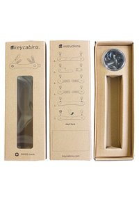 Emballage Keycabins avec trois sections : carton brun, fenêtre transparente, instructions d'assemblage illustrées et un contenant circulaire avec des vis.