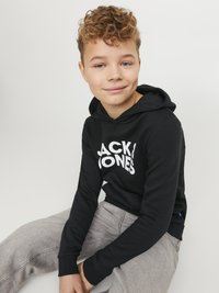 Črna kapuca z belim tiskom, ki prikazuje ime blagovne znamke, v kombinaciji s svetlo sivoh hlaci. Kapuca ima sprednji kenguru žep in rebraste manšete.