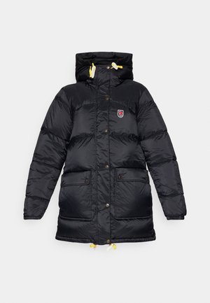 Zwarte pufferjack met een hoge kraag, twee voorzakken, gele trekkoorden en een logopatch op de borst. Glad, glanzende textuur.